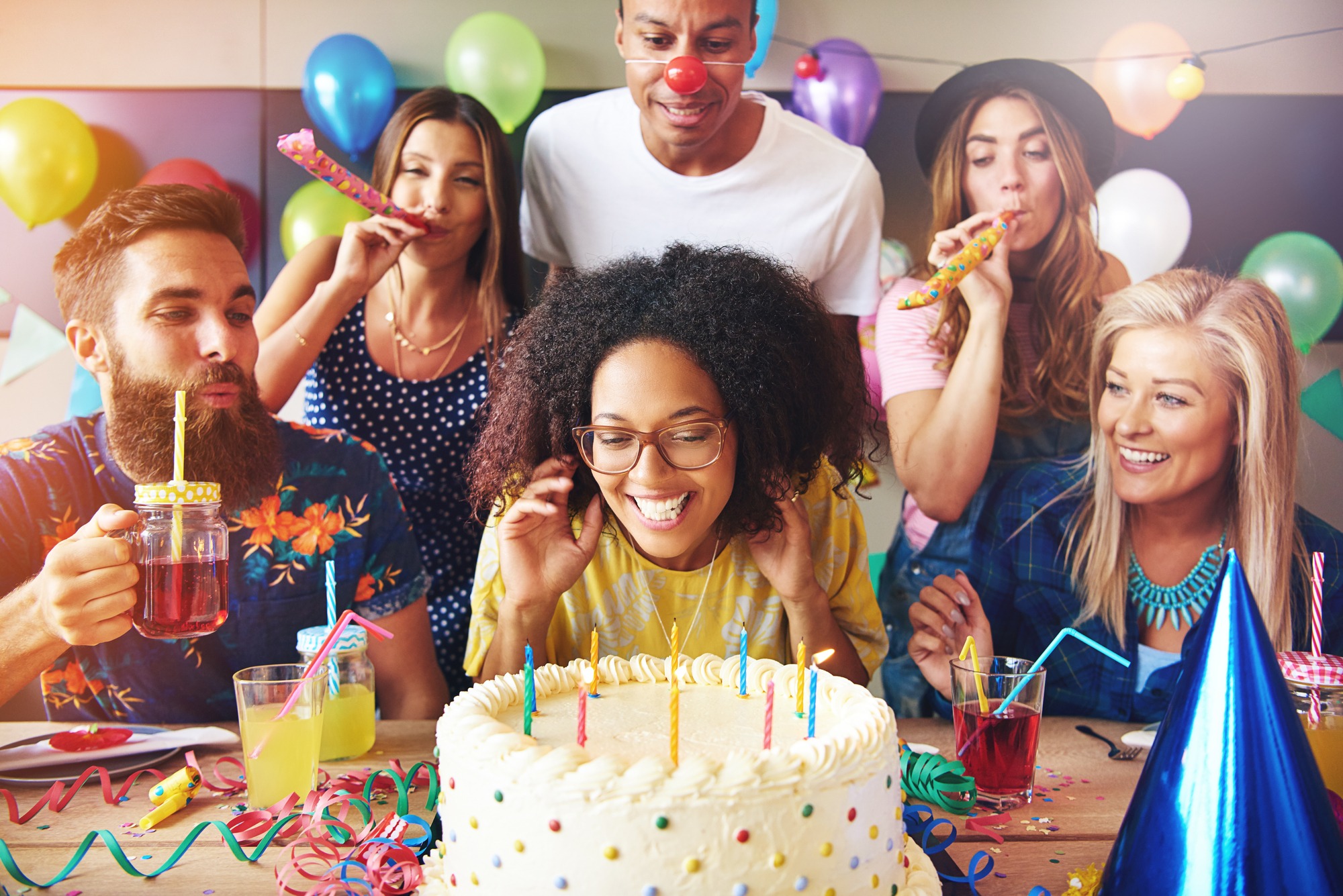 Excited woman ready to blow out candles on white frosting cake on table at birthday party with happy friends